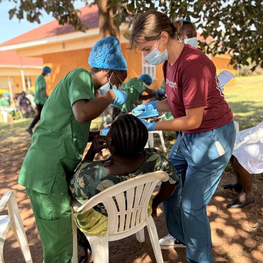 A Ugandan dental student and a visiting volunteer treating a patient together outdoors